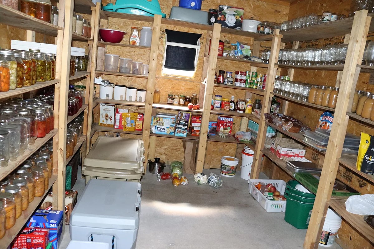 A well-stocked Amish pantry with rough shelving full of home-canned jars and coolers