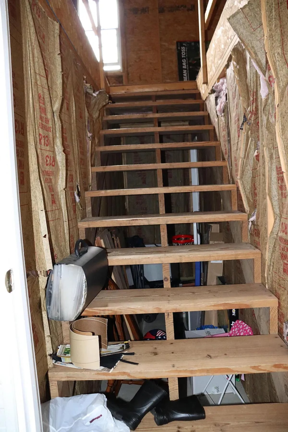 A raw unfinished stairway with exposed framing and fiberglass insulation leading upstairs