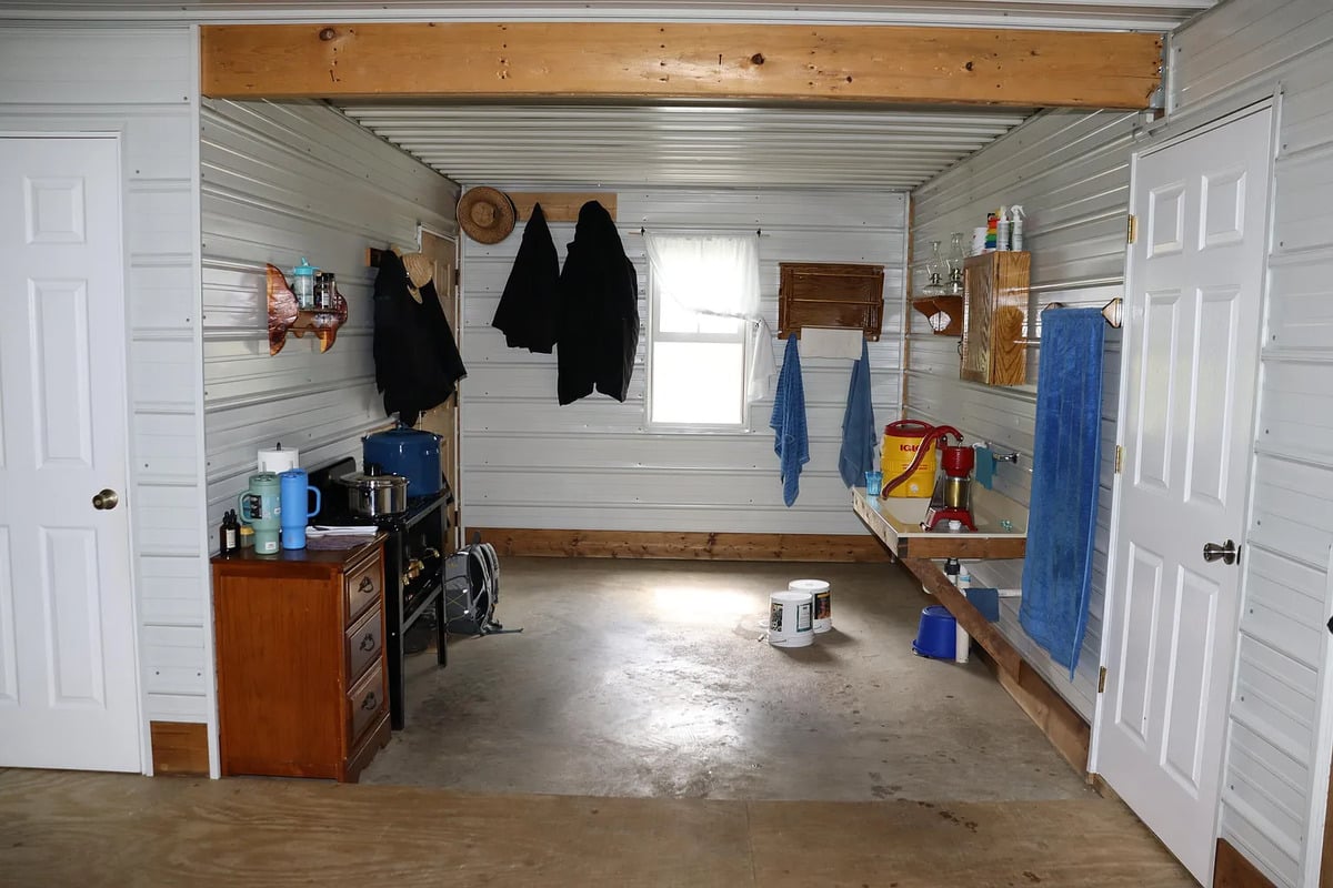 An Amish wash room with coats and a straw hat on wall pegs, blue towels, and a water cooler on a counter