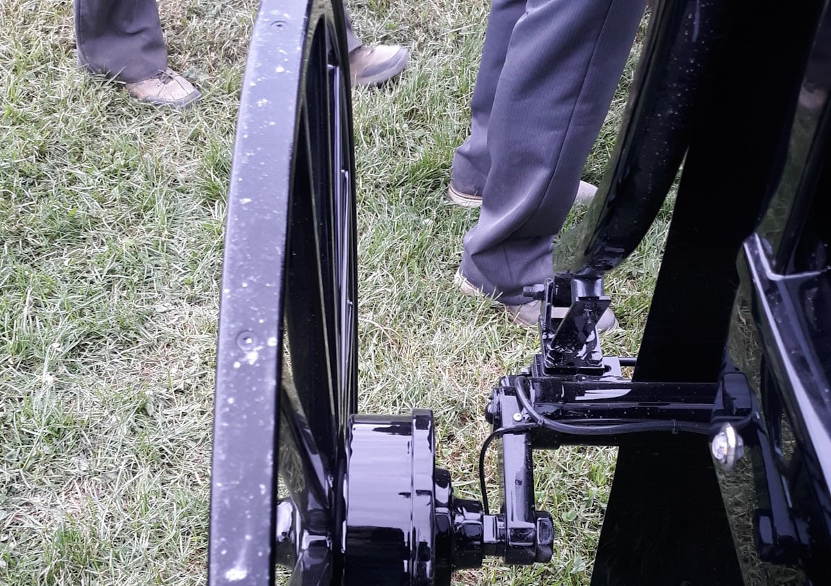 Close-up of the metal hub and wheel of an Amish buggy on grass, with two Amish men standing beside it