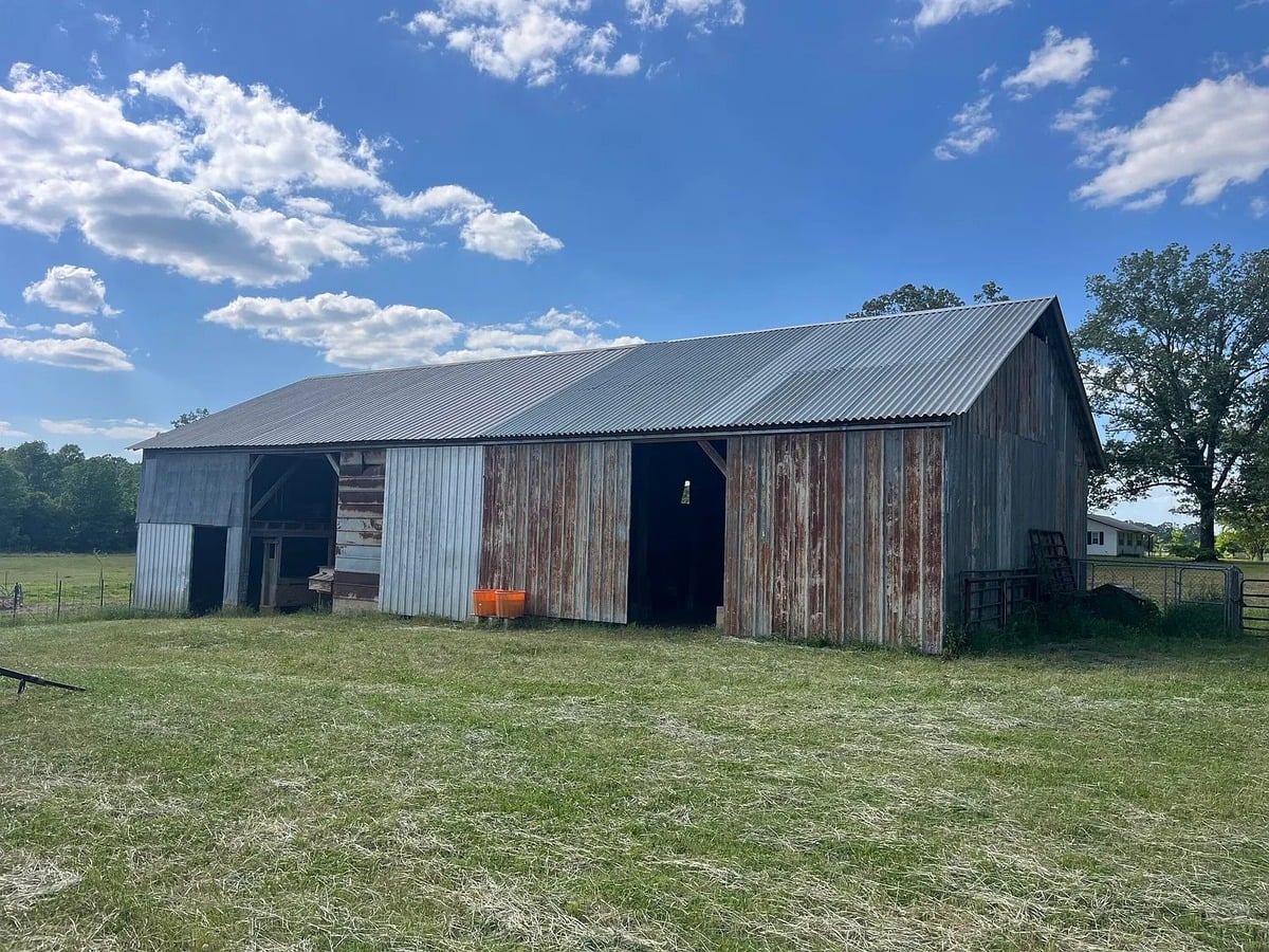 Large weathered Amish barn with corrugated metal roof and rusted vertical siding and open bays, Randolph Mississippi