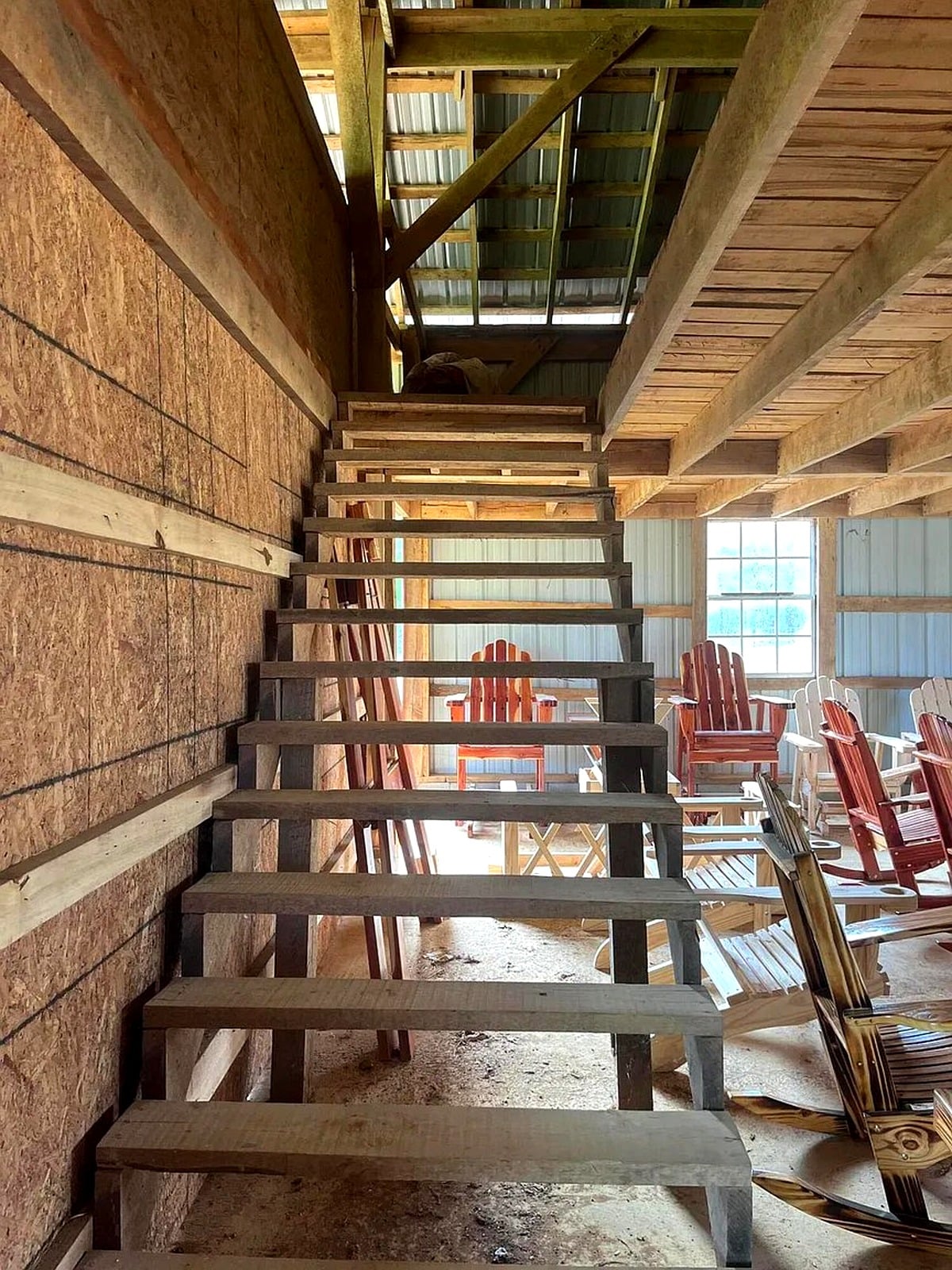 Staircase inside Amish furniture shop leading to upper loft, with chairs visible below
