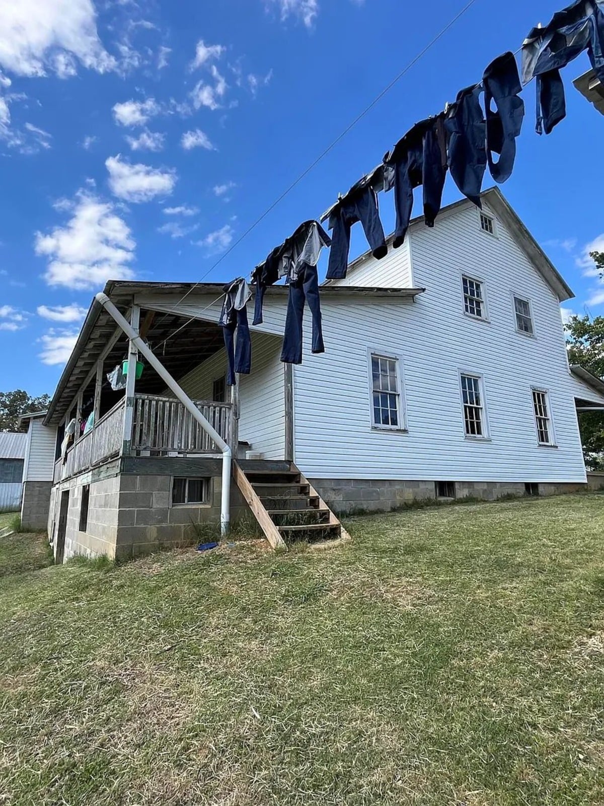 Dark Amish clothing on clothesline with two-story white Amish farmhouse in background, Randolph Mississippi