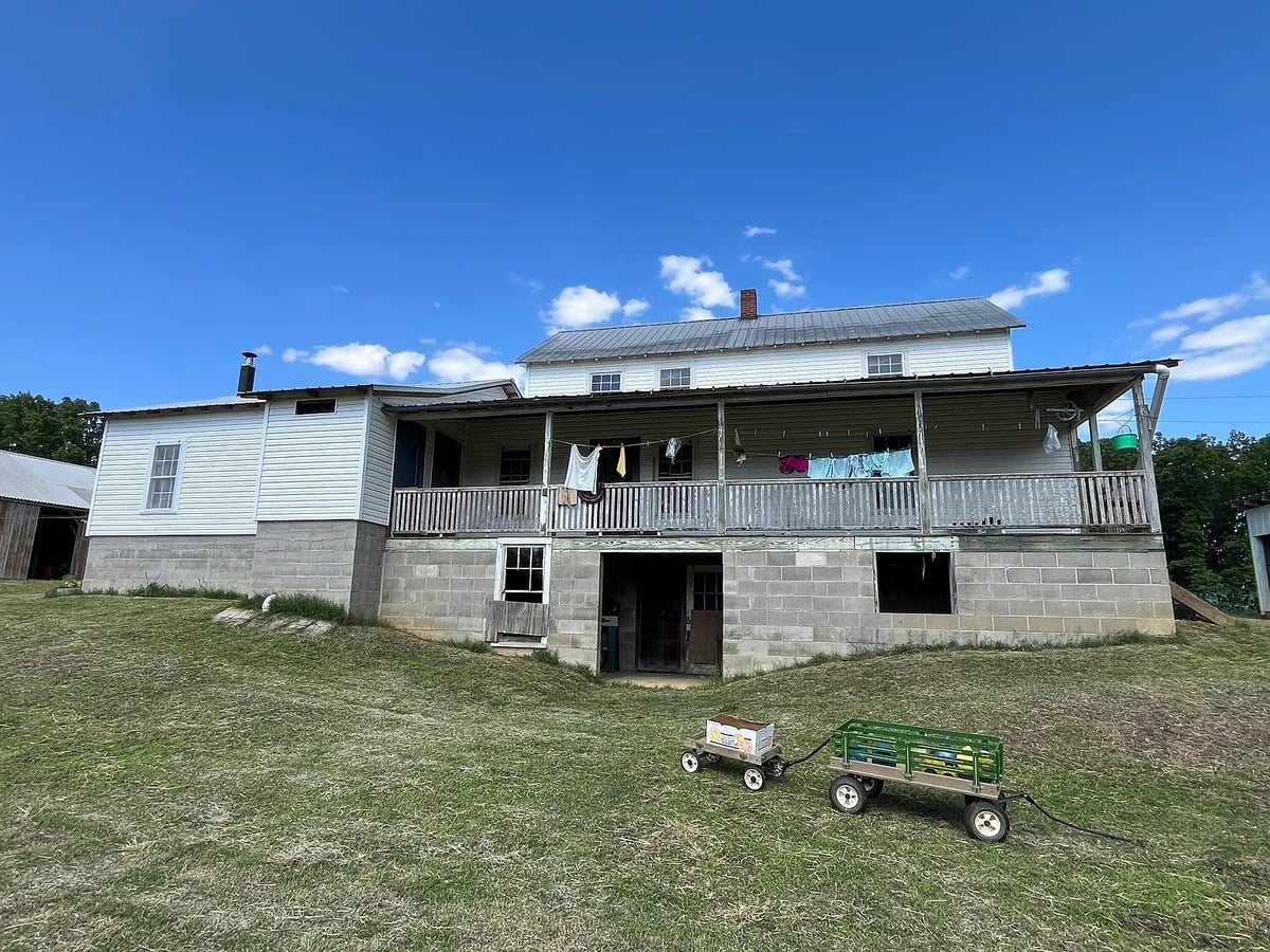 Rear view of two-story Amish home showing cinder block foundation, back porch with laundry, and two wooden wagons in yard