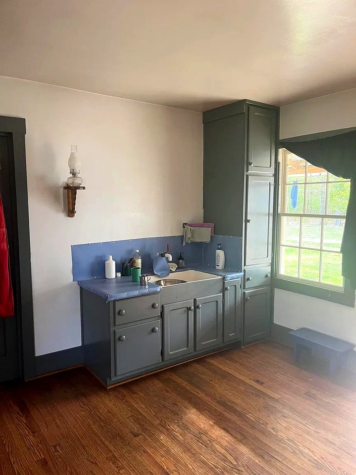 Blue-green kitchen cabinets and farmhouse sink in an Amish home in Mississippi, with oil lamp wall sconce