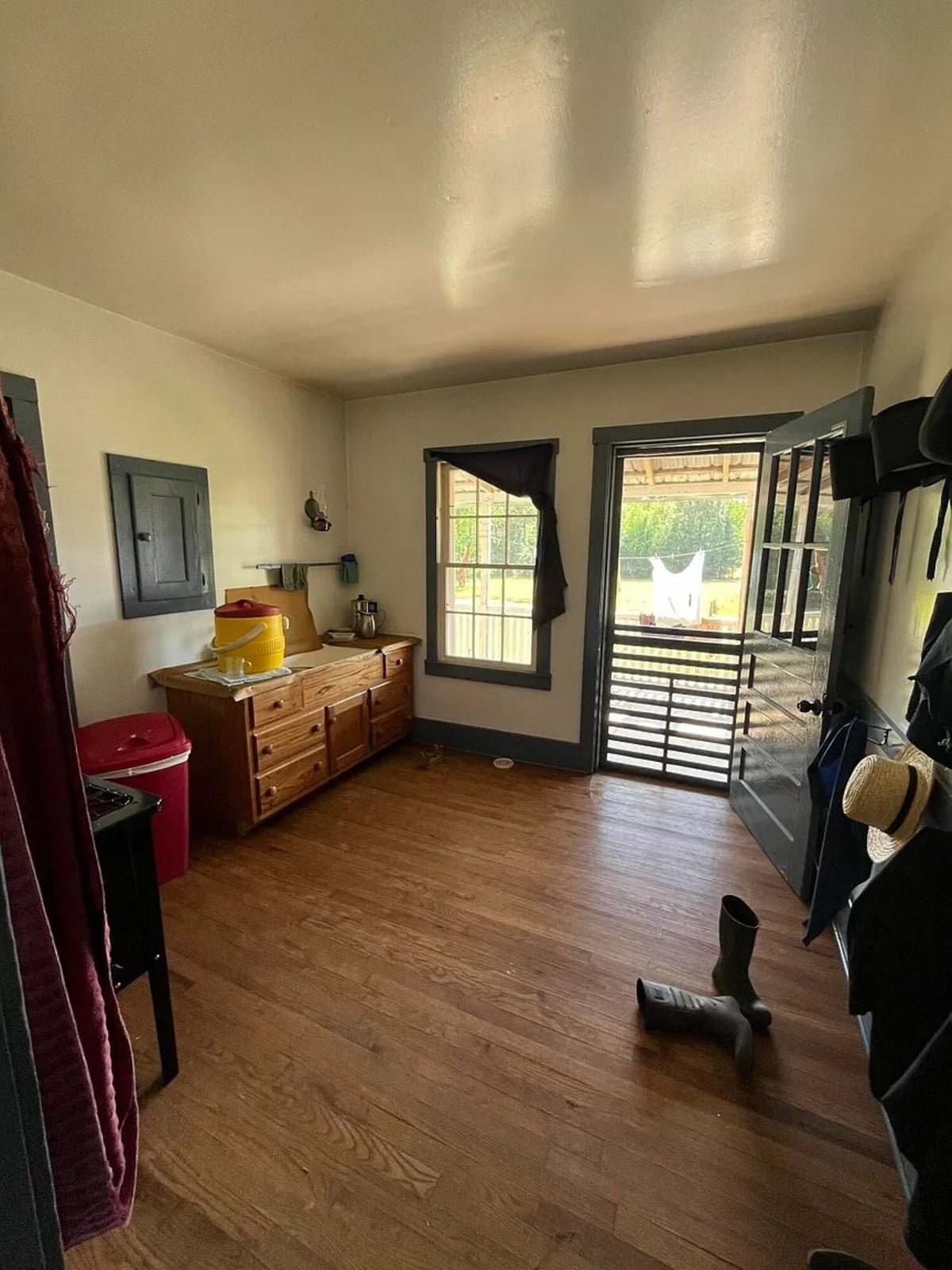Amish mudroom with rubber boots, straw hat, dark coats on hooks, and wooden dresser, Randolph Mississippi