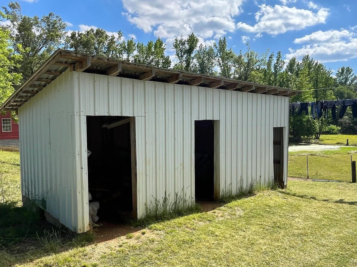 Small white metal Amish outbuilding with open bays and dark Amish clothing on clothesline behind it, Randolph Mississippi