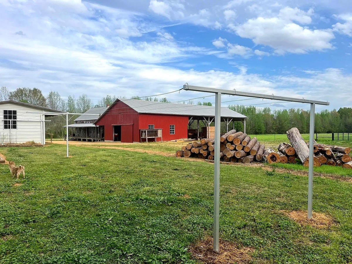 Red Amish barn with log pile and metal clothesline posts in Randolph, Mississippi