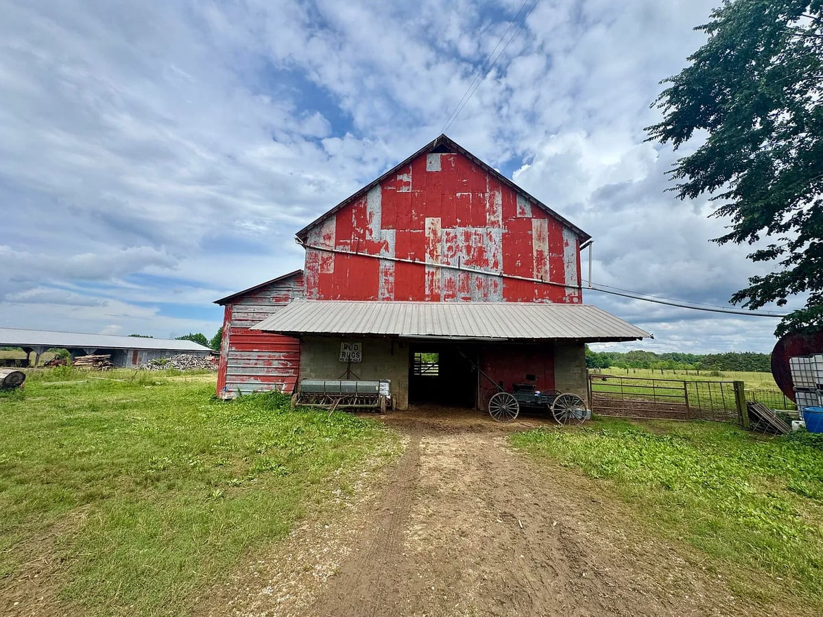 Weathered red Amish barn with rugs sign, buggy, and seed drill in Randolph, Mississippi