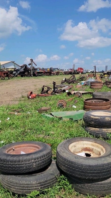 Used tires, rims, axles and equipment parts laid out in rows in the grass