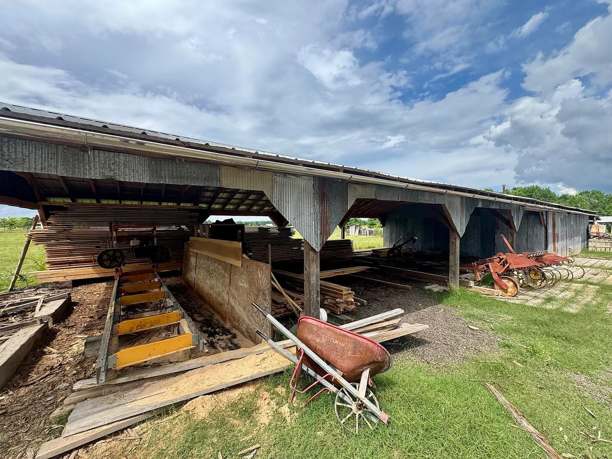 Portable sawmill and stacked lumber under a pole shed on an Amish farm in Randolph, Mississippi