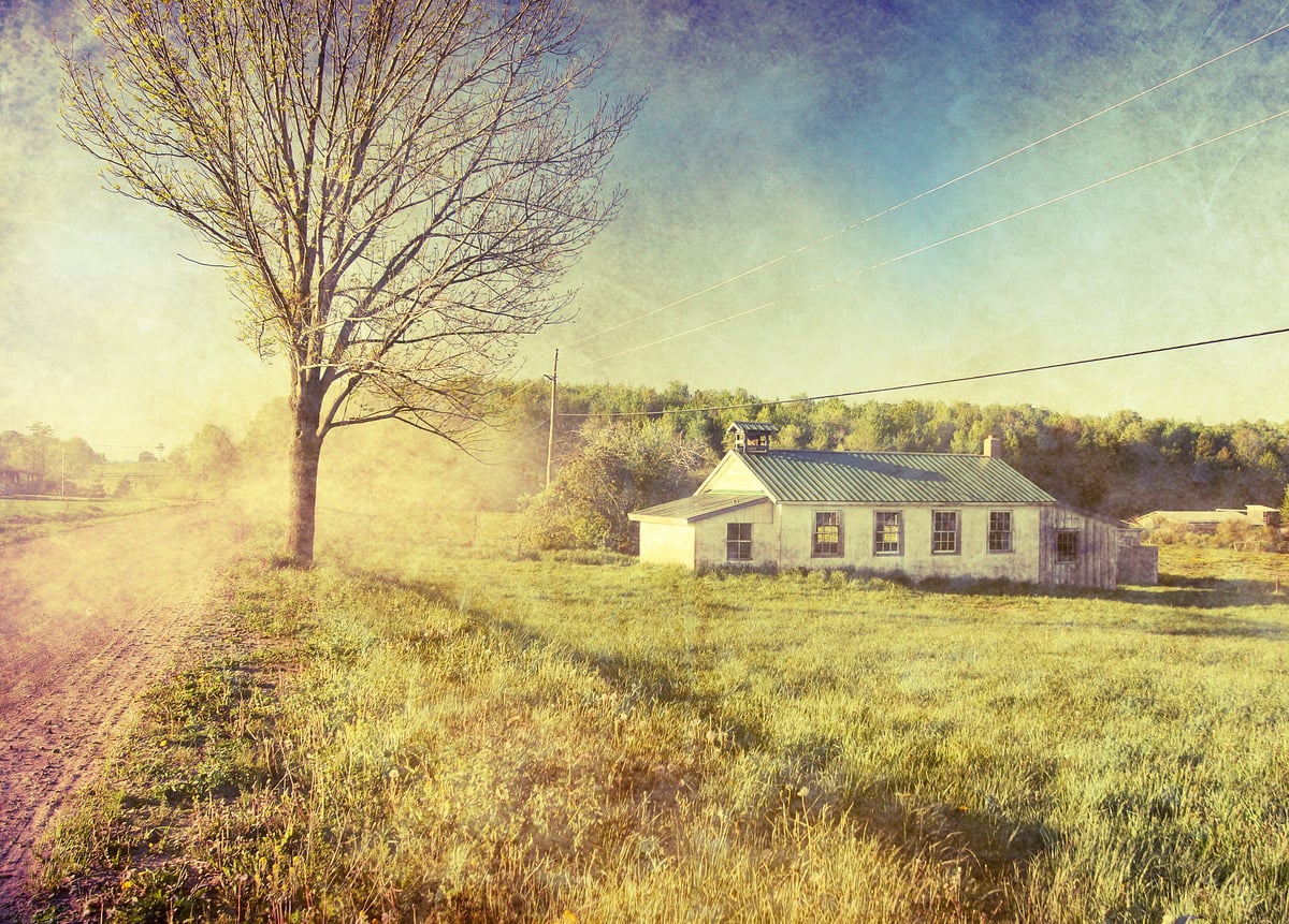 White one-room schoolhouse with a bell cupola and green metal roof beside a dirt road in Sugar Grove, Pennsylvania