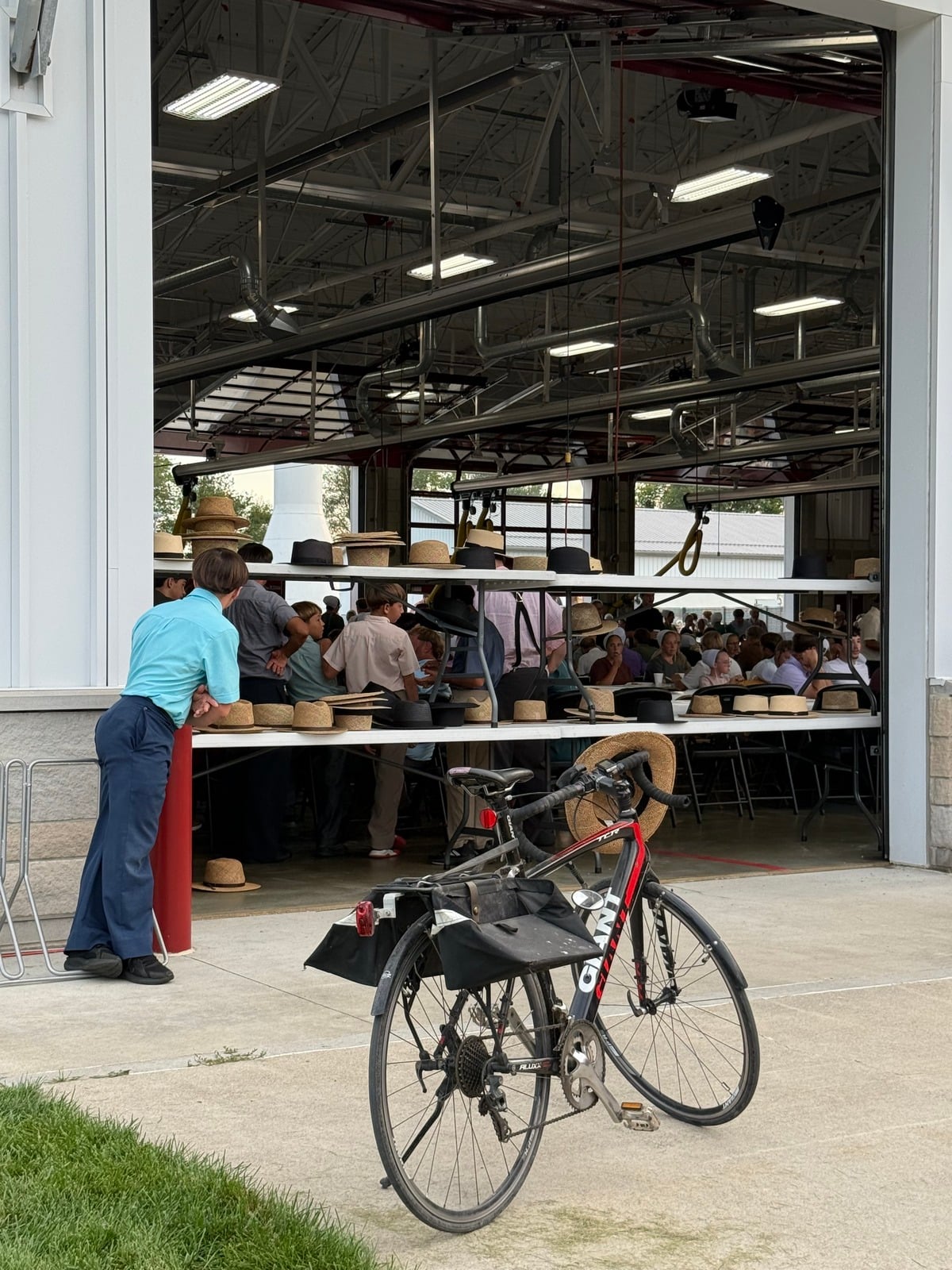 Amish boy leaning on a post by a table of hats at the fire station bay door