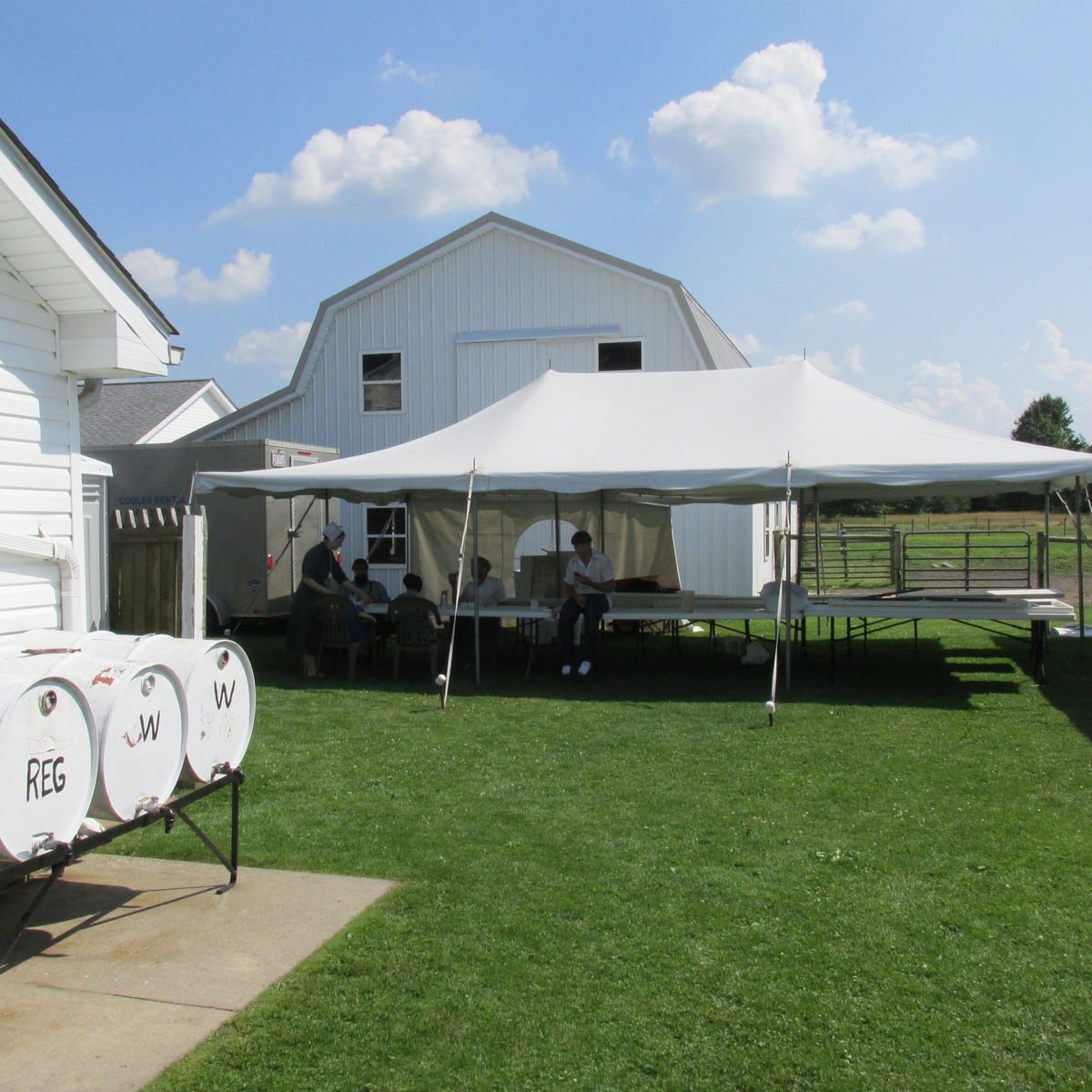 Wedding tent beside a white barn with dispenser barrels in the foreground