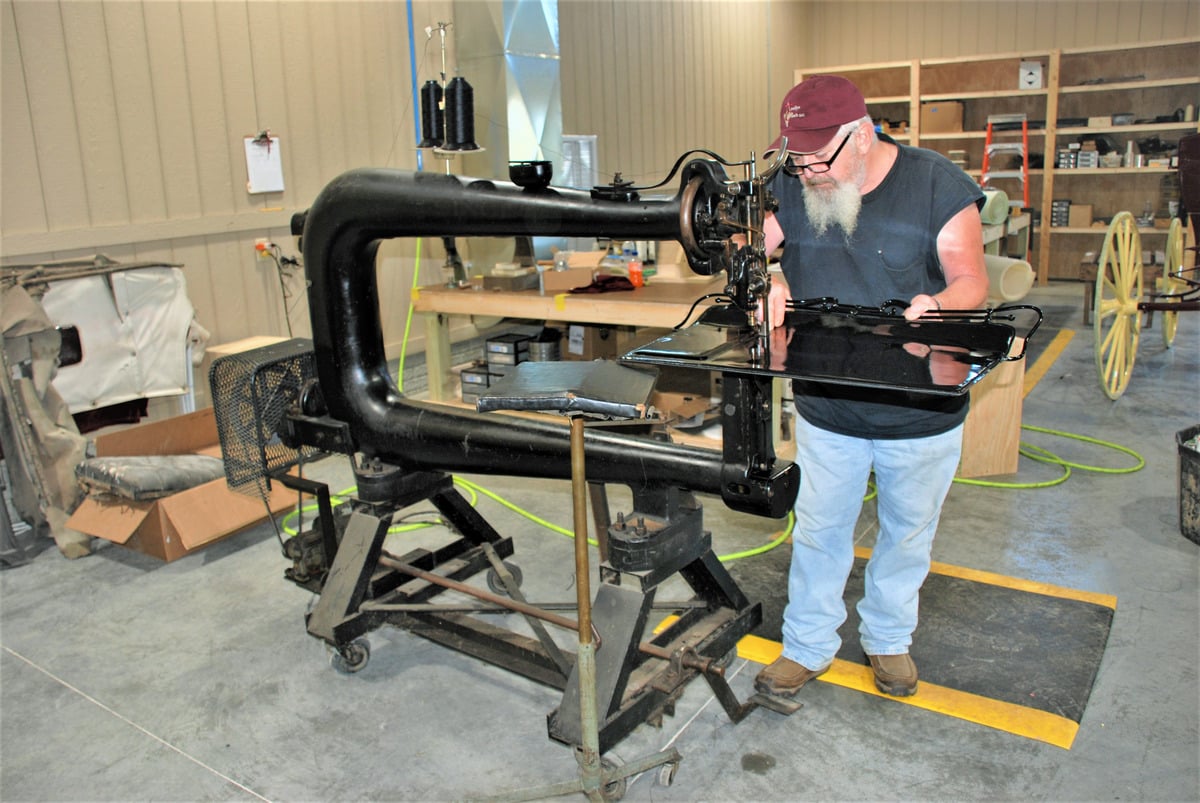 Shop worker feeding a black carriage top through a large 1904 Singer sewing machine