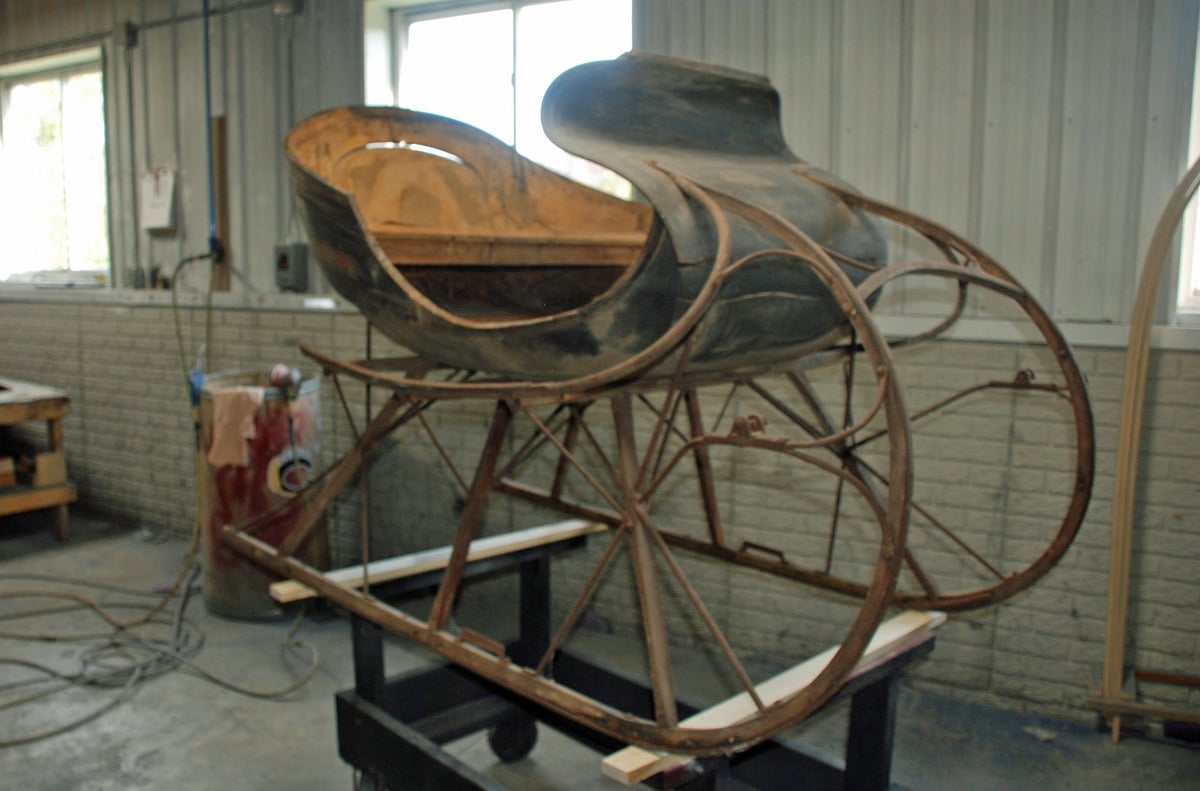 Stripped and rusted sleigh body and runners sitting on a shop cart before restoration