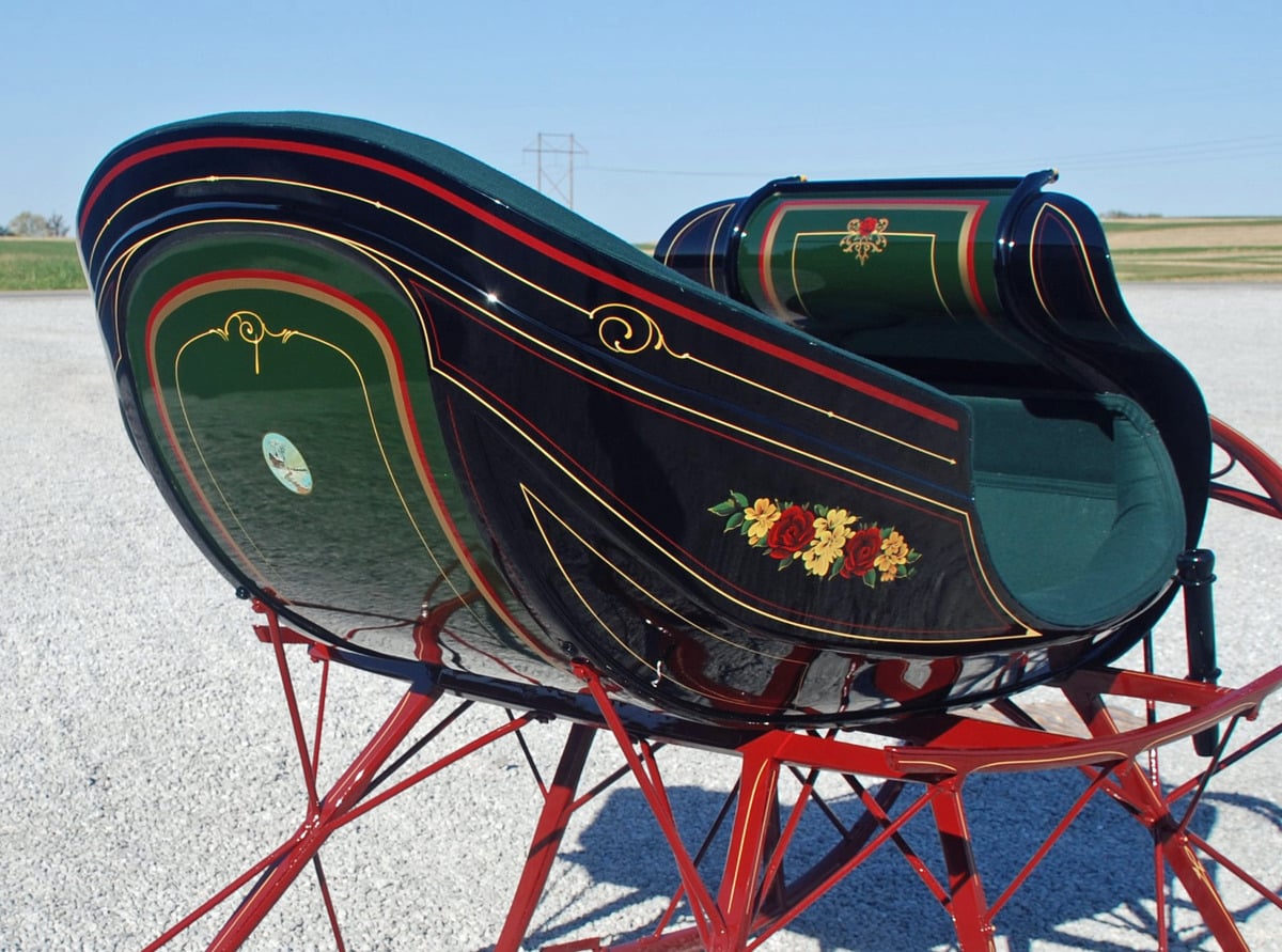 Close view of painted roses, gold striping and green upholstery on a restored sleigh