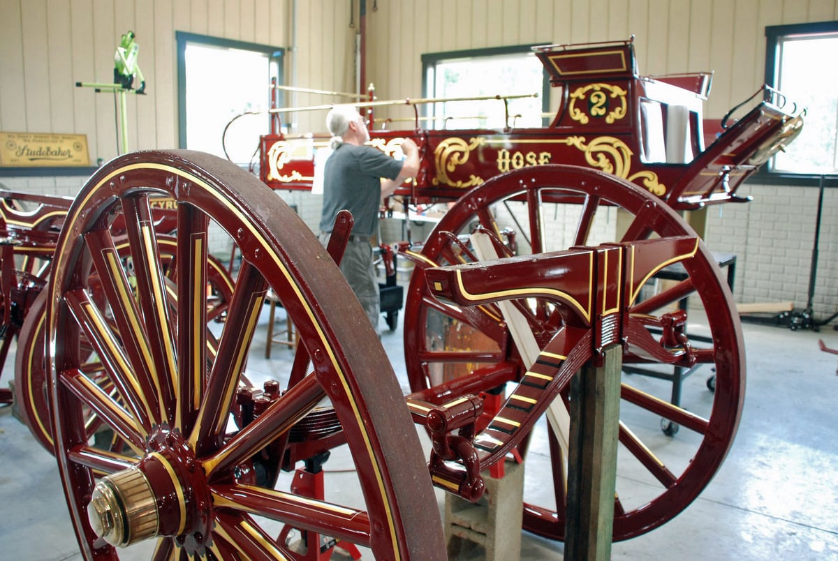 Wagon wheels with gold pinstriping in the foreground, Wayne Troyer painting a hose wagon behind them
