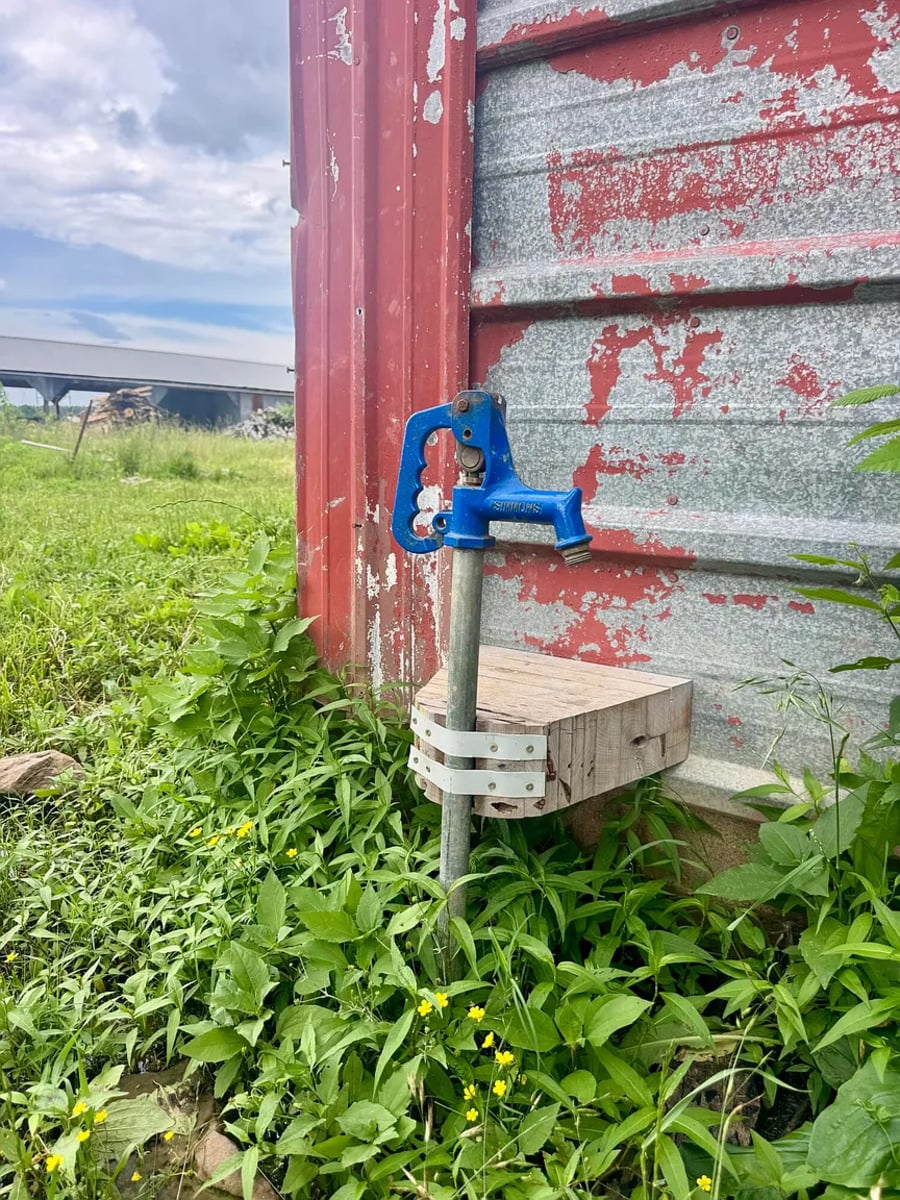 Blue yard hydrant beside a weathered red barn on an Amish farm in Mississippi